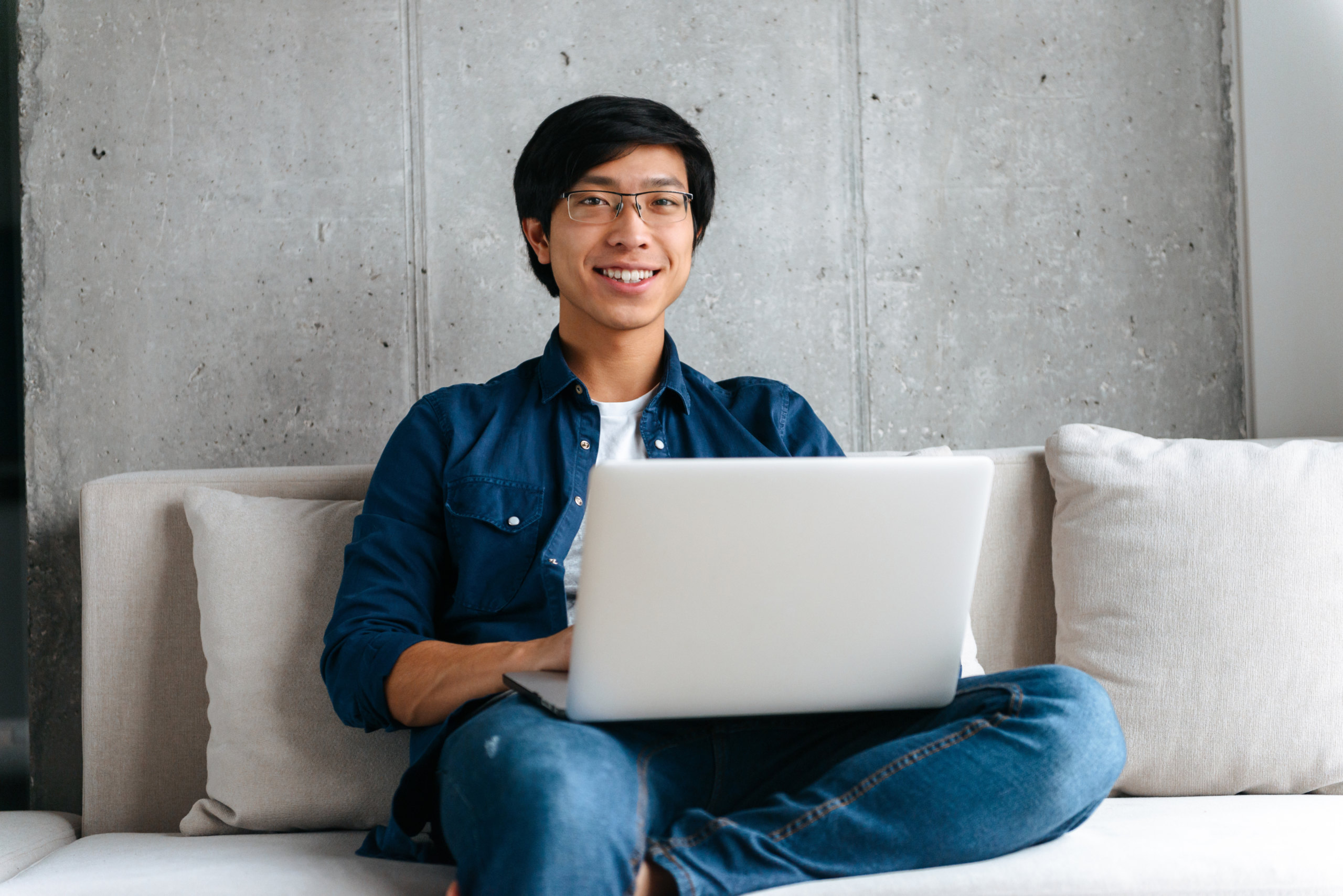 asiatischer junger Mann sitzt mit Labtop auf dem Sofa
